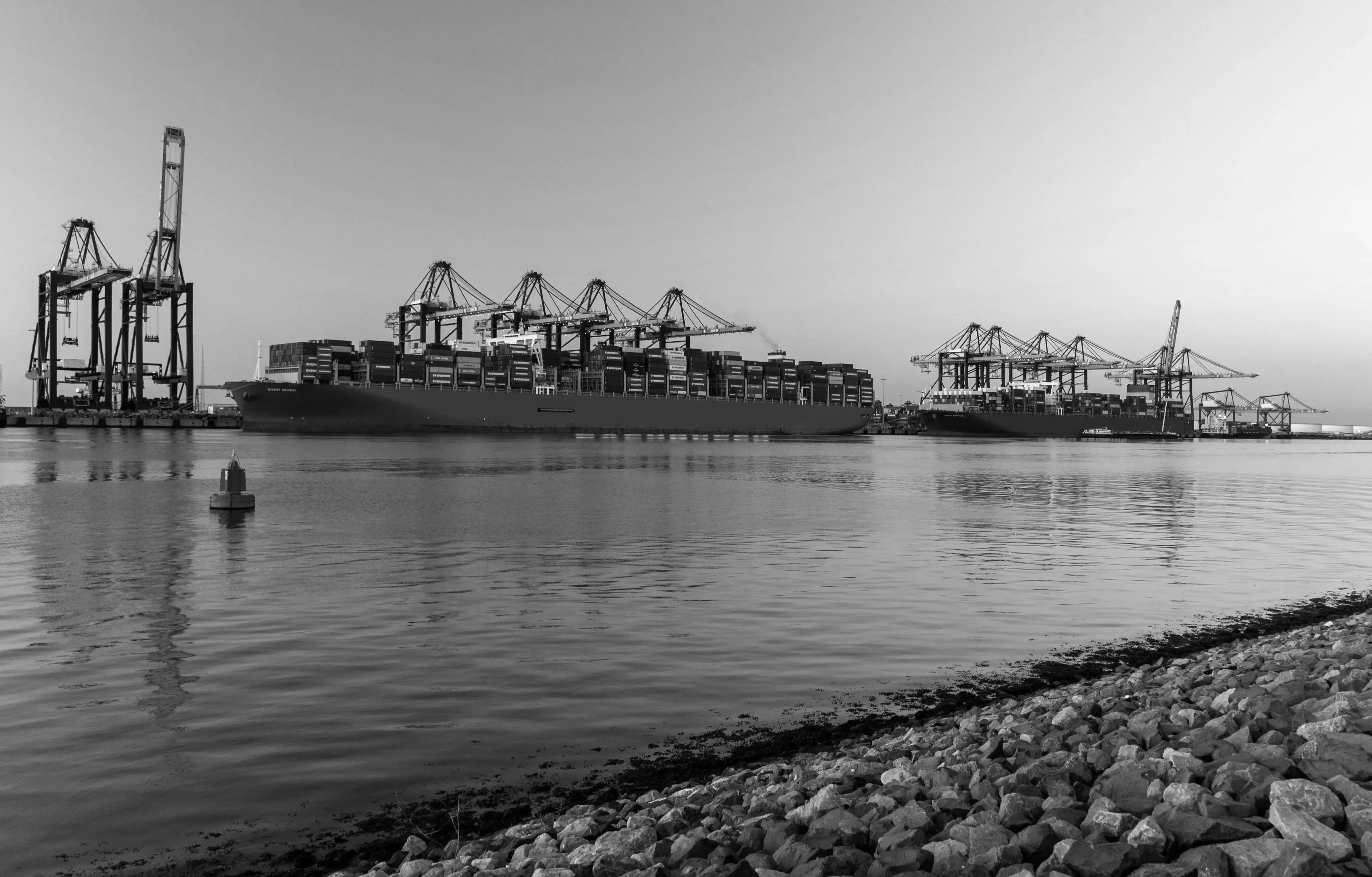 Aerial view of a large cargo ship docked at a port, with cranes and containers visible, representing global logistics and shipping.